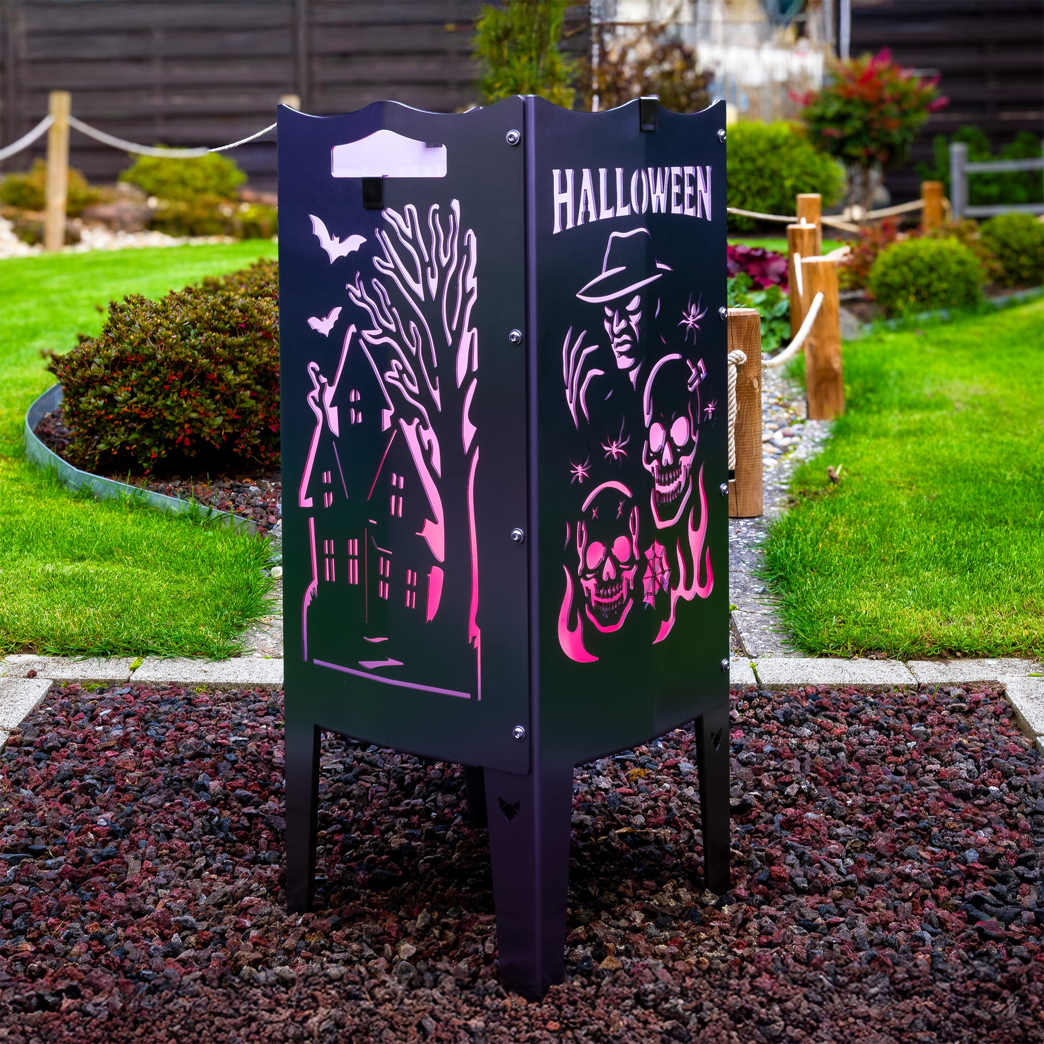 Die FENNEK Halloween Feuersäule lt. Edition steht in einem schönen Garten  und wird mit LED-Strahler von Innen beleuchtet. Der Feuerkorb kann aber auch mit normalem Feuer betrieben werden. Made in Germany.