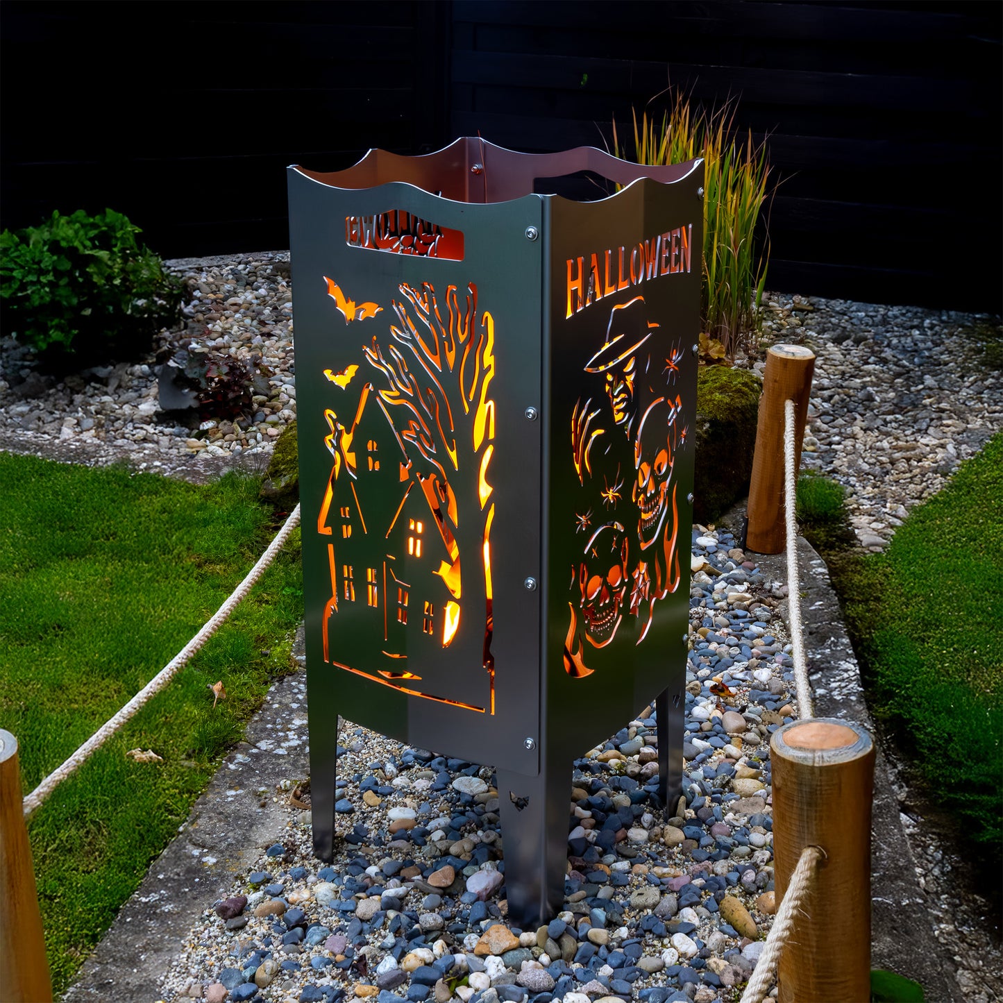 Die FENNEK Halloween Feuersäule lt. Edition steht in einem schönen Garten und wird Feuerholz von Innen beleuchtet. Der Feuerkorb kann aber auch mit einem LED-Strahler von Innen betrieben werden. Made in Germany.