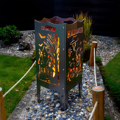 Die FENNEK Halloween Feuersäule lt. Edition steht in einem schönen Garten und wird Feuerholz von Innen beleuchtet. Der Feuerkorb kann aber auch mit einem LED-Strahler von Innen betrieben werden. Made in Germany.