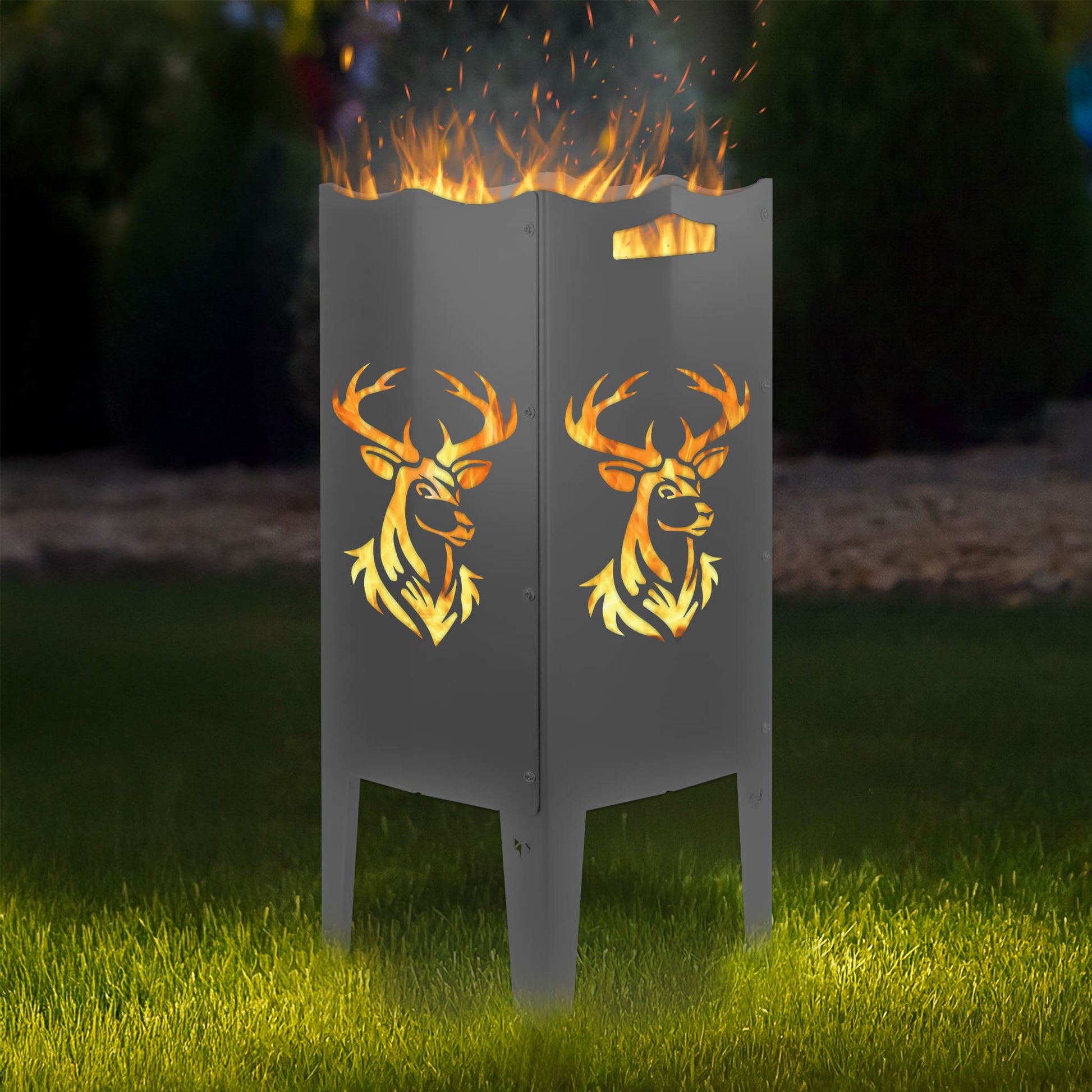 FENNEK Feuersäule Stahl mit dem Motiv Hirsch - in der Feuersäule brennt ein Feuer, man sieht das Motiv sehr schön leuchten in der Abenddämmerung in einem Garten. Die Feuersäule steht auf Gras.