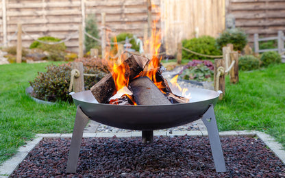 Ein schönes Lagerfeuer in der Feuerschale Edelstahl, welche auf einem Kiesbett steht in einem schön angelegten Garten..