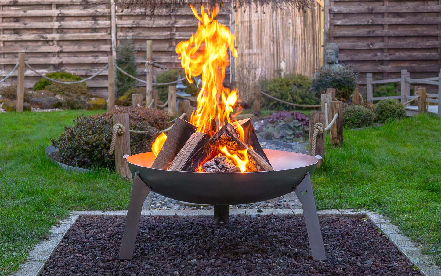 Ein schönes Lagerfeuer in der Feuerschale Edelstahl, welche auf einem Kiesbett steht in einem schön angelegten Garten..