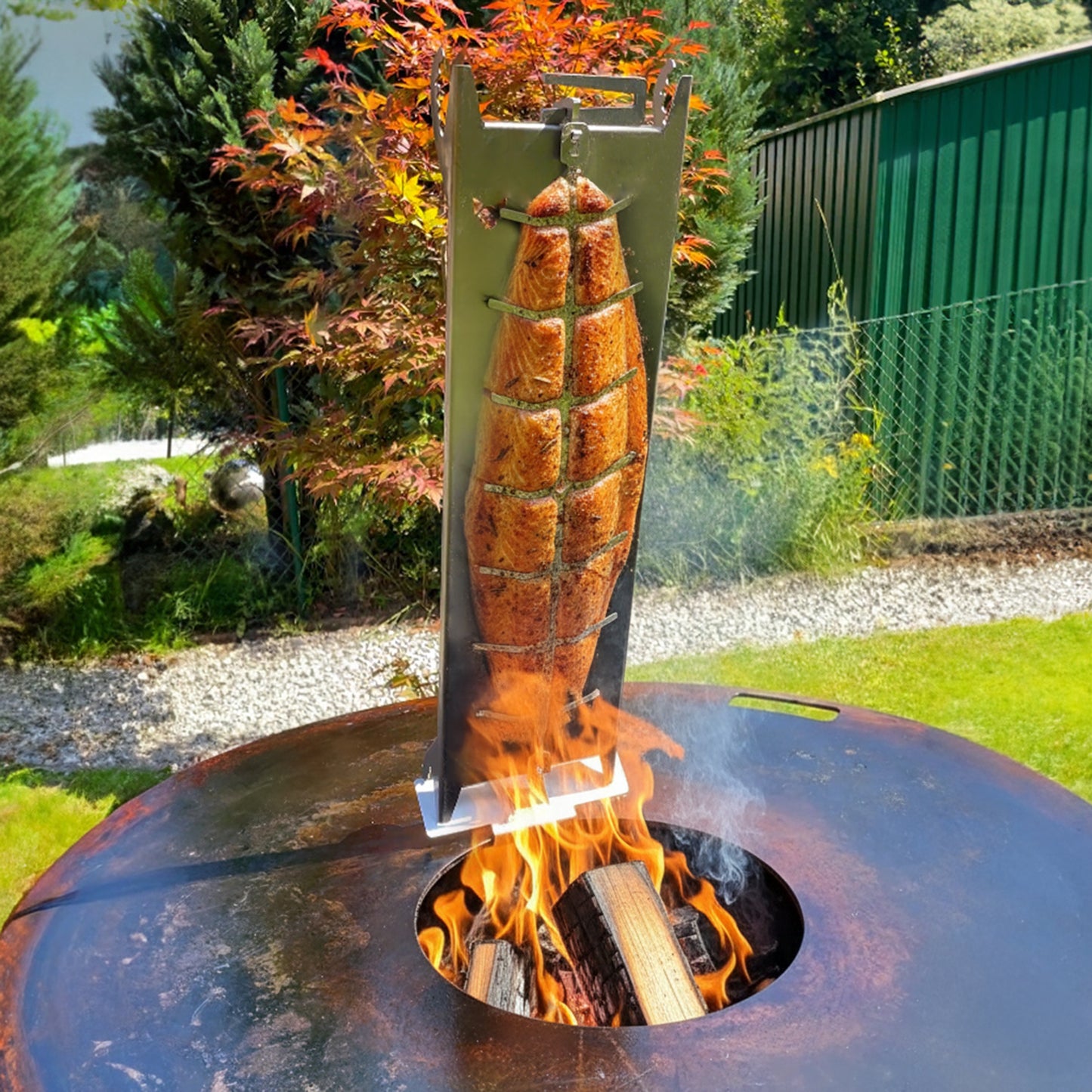 Bild einer Szene bei der der FENNEK Flammlachshalter aus Edelstahl auf dem Feuerplattenadapter für Flammlachshalter an der Feuerplatte befestigt ist. Auf dem lachsbrett ist ein schönes, saftiges Stück Lachs angebracht. Aus dem Loch der Feuerplatte lodern Flammen.