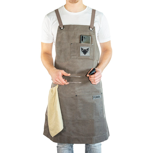 Grillschürze mit FENNEK Logo-Applikation und FENNEK-Schriftzug an männlichem Model mit weißem T-Shirt getragen. Grillzange und Feuerzeug in den Händen, ein Lappen in der seitlichen Tasche und Smartphone in der Brusttasche.