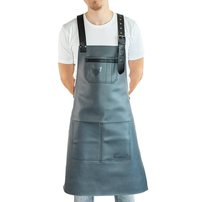 Brustbereich Leder-Grillschürze mit geprägtem FENNEK-Logo und mit verstellbarem Lederriemen, Schnalle und aufgesetzten Taschen, getragen von einem Mann