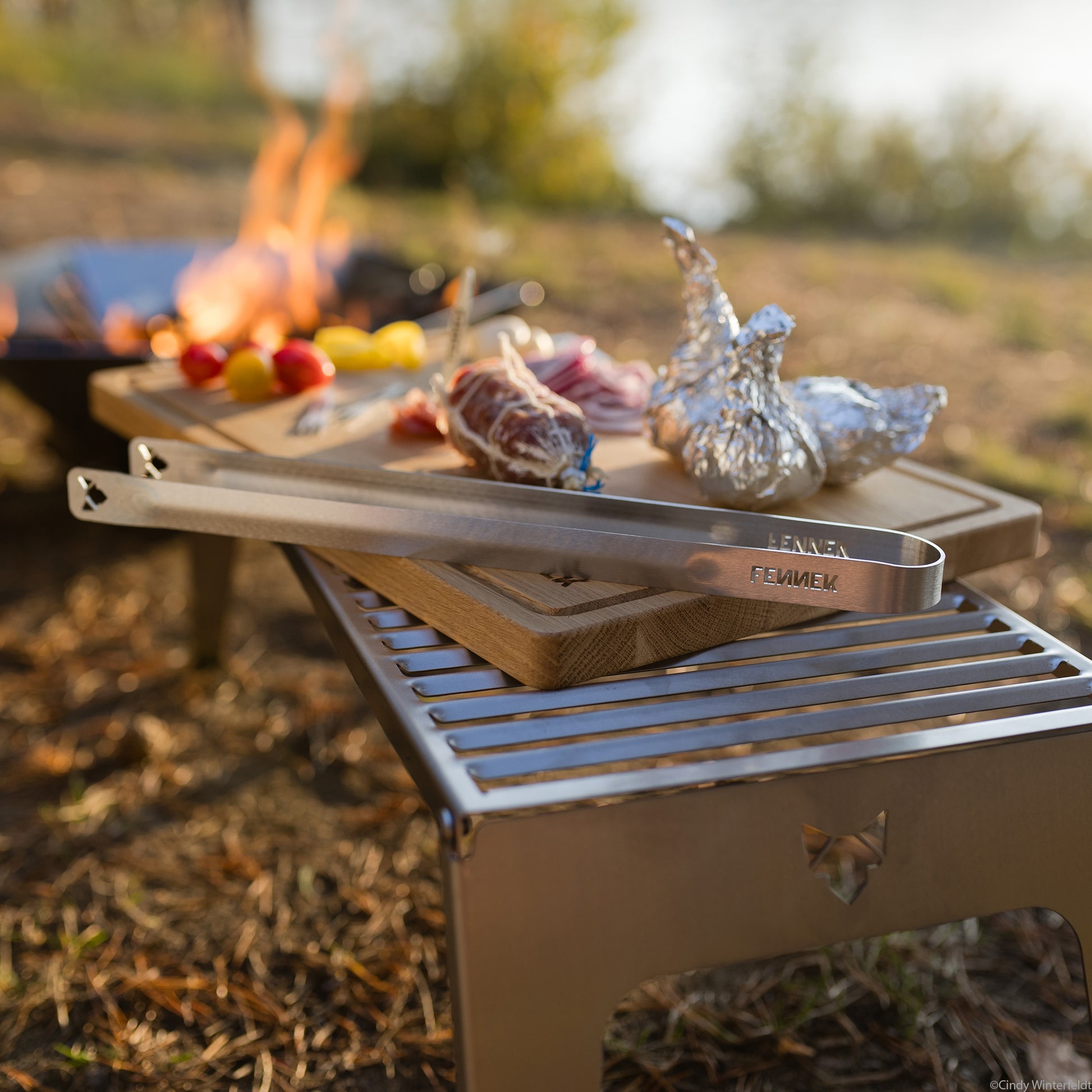FENNEK Grillzange klein liegt auf dem FENNEK Scheidebrett, welches auf dem Klapprost XL platziert ist.