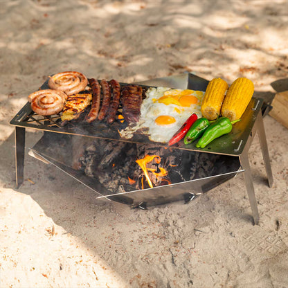 Die FENNEK Feuerschale Hexagon steht am Strand am See. Darüber ist der FENNEK 4fire aufgestellt, auf welchem 1 Steak, 3 Merguez, 2 Bratwurstschnecken, 1 Hähnchenbrustfilet, 2 Spiegeleier, 1 rote Paprika, 2 grüne Paprika und 2 Maiskolben gegrillt wird. 