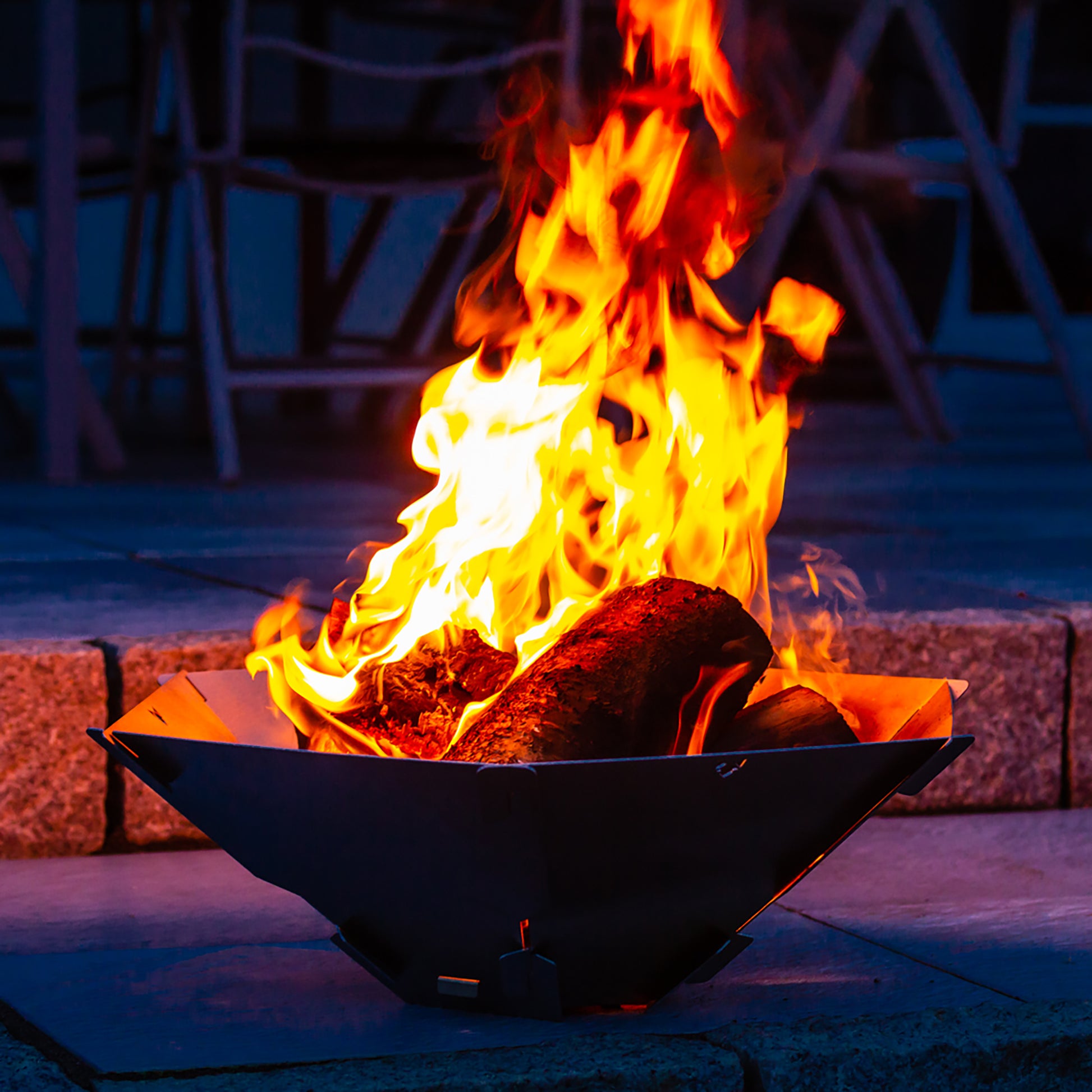 Brennendes Feuer in der Feuerschale Hexagon bei Dunkelheit auf einer Steinterasse.