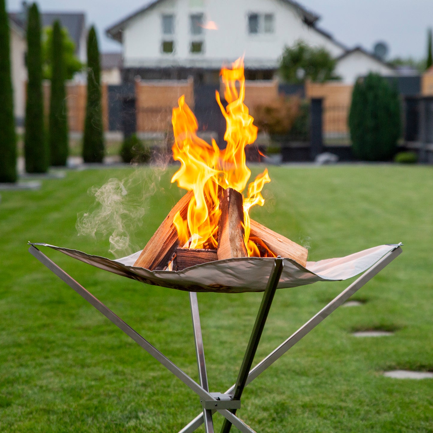 Brennendes Feuer auf dem Feuernetz im Garten mit grünem Rasen im Hintergrund