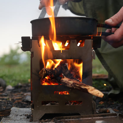 Hobokocher mit brennendem Holz im Einsatz, darauf eine Pfanne in der gerade Essen zubereitet wird in der Natur