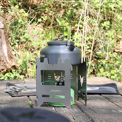 Hobokocher am Tisch einer Sitzgruppe im Wald, nicht ganz geschlossen, als Windschutz um einen Gaskocher gestellt, auf dem ein Wasserkessel zum kochen gebracht wird.