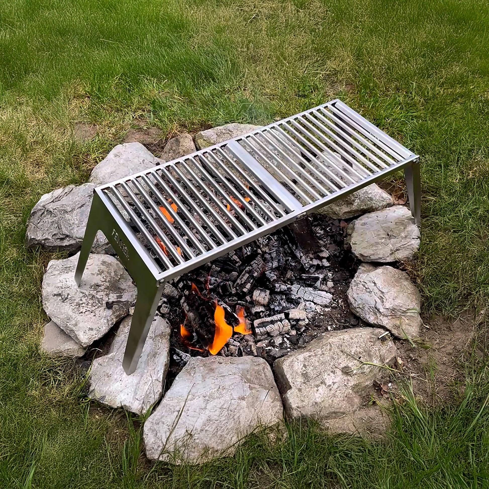 Der FENNEK Klapprost XL steht auf einer Feuerstelle in dem Feuer brennt und heiße Glut liegt. Der Edelstahl Klapprost zeichnet sich durch seine Feuerfestigkeit aus, sodass ihm die Flammen nichts anhaben können.