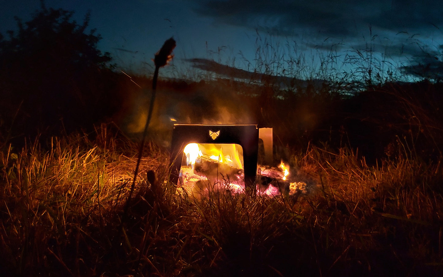 FENNEK Klapprost XL über Lagerfeuer in einem Feld in abendlicher Stimmung. 