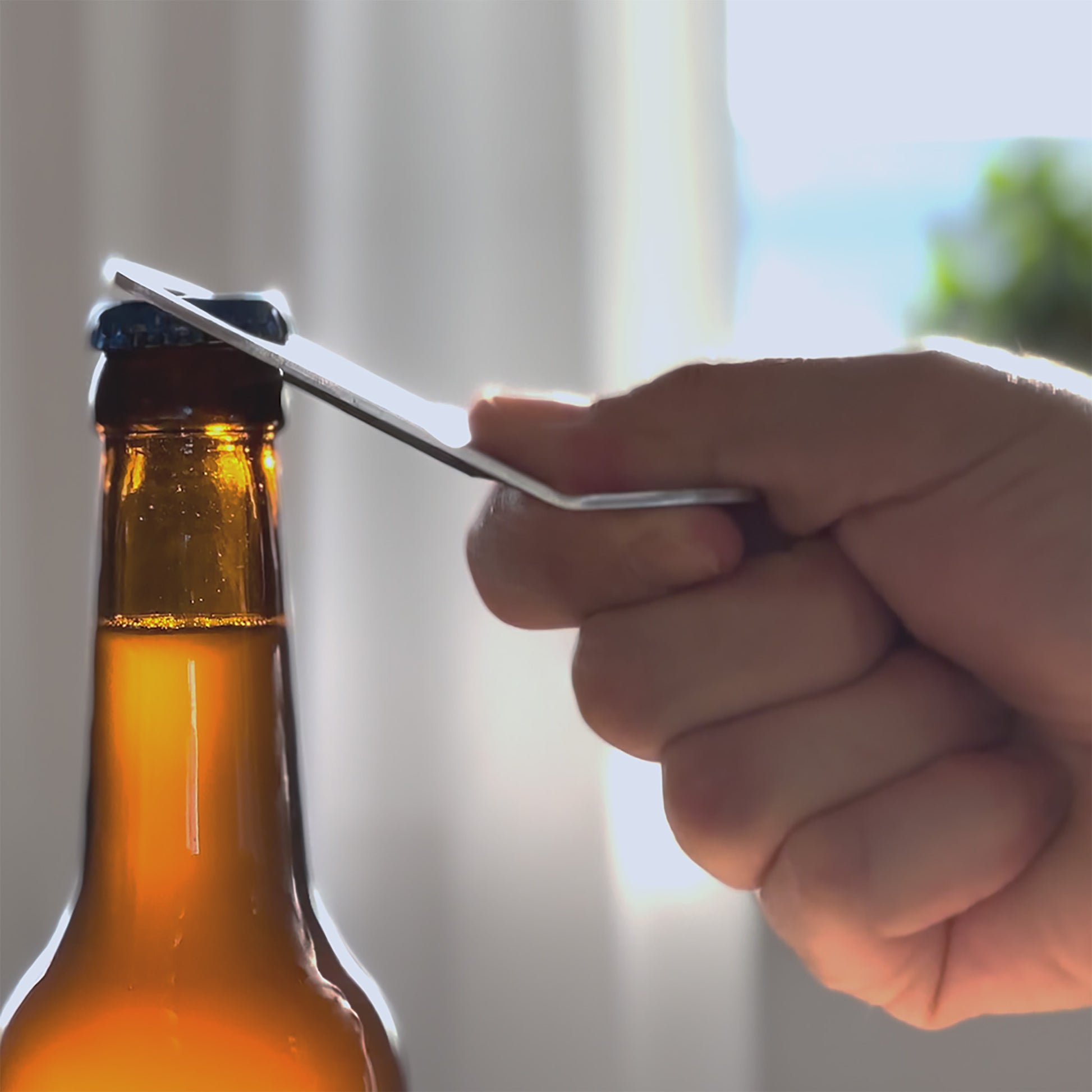 Eine Hand öffnet mit dem FENNEK Flaschenöffner Captain Cork Magnetisch Mobil eine Bierflasche.