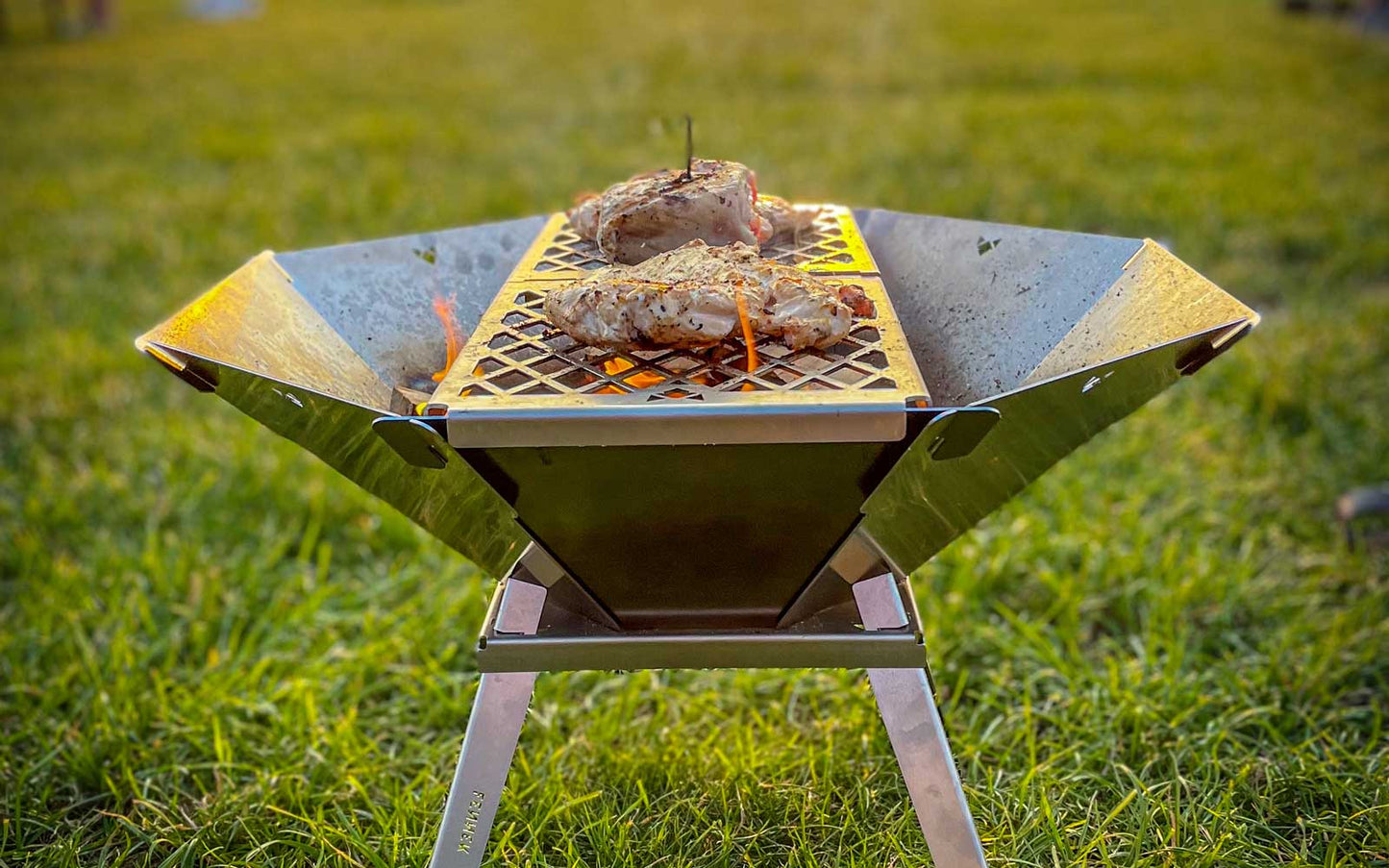 gegrilltes Fleisch auf dem Grillrost für die Feuerschale Oktagon, stehend auf einer grünen Wiese.