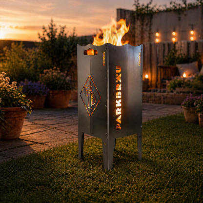 Szenebild zeigt die FENNEK Feuersäule mit dem Parkbräu Logo befeuert in einem Garten bei schönem abendlichen Licht. Sie ist perfekt für alle Fans, Sammler und Bierliebhaber. Das unverwechselbare Parkbräu Logo ist präzise ausgeschnitten und sorgt befeuert für ein unverwechselbares Erlebnis.