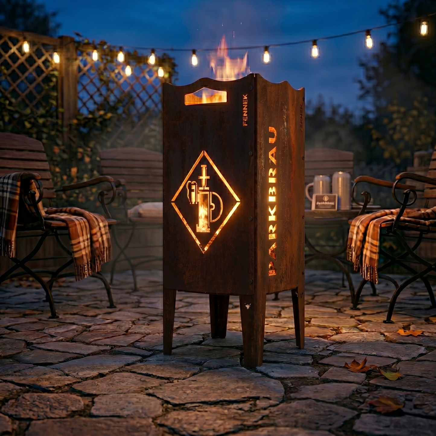 Die FENNEK Feuersäule mit dem Parkbräu Logo steht auf der Terrasse bei schönem abendlichen Licht. Ein warmes Feuer lodert und sorgt für eine gemütliche Stimmung. Die Säule aus Stahl hat eine schöne Rostoptik und eignet sich somit perfekt als rustikaler Eyecatcher.