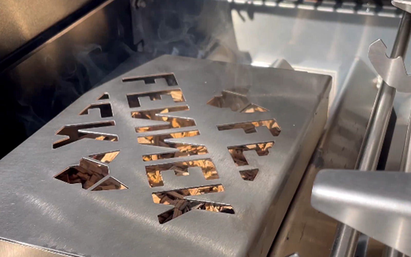 Bildausschnitt zeigt die FENNEK Räucherbox auf den Aromablechen von einem Gasgrill.
