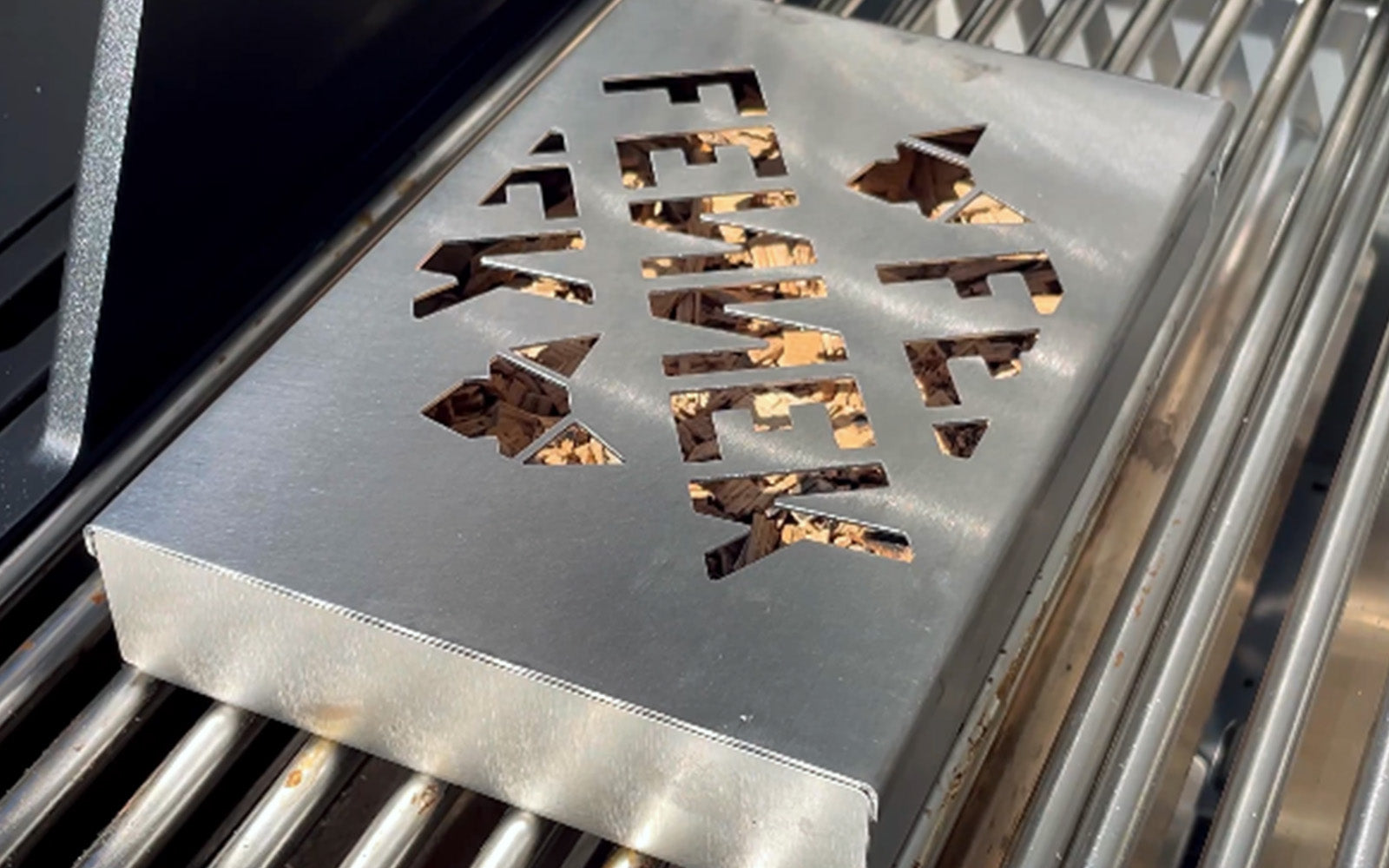 Bildausschnitt zeigt die FENNEK Räucherbox auf dem Grillrost von einem Gasgrill.