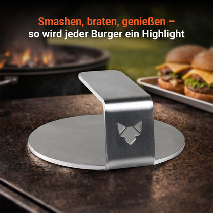 Bild zeigt den FENNEK Burger Smasher. Im Hintergrund sieht man einen Kugelgrill und daneben ein paar fertige Burger. Durch die Verwendung des FENNEK Burger Smashers wird jeder Burger ein Highlight.