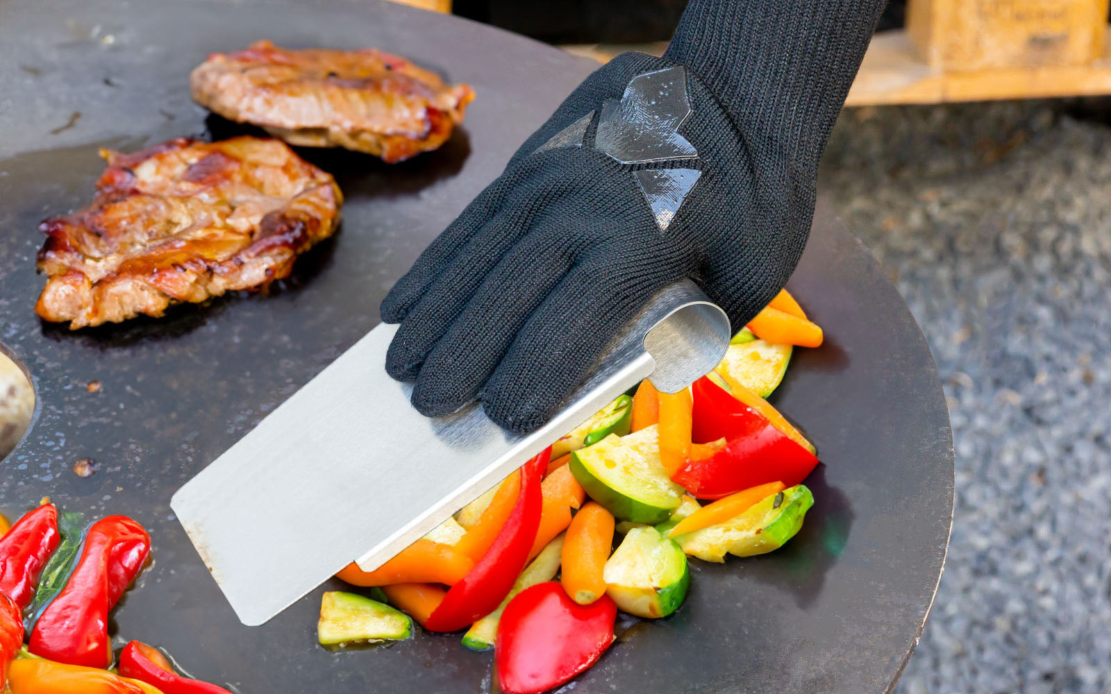 Bild zeigt wie der FENNEK Grillspachtel auf der Feuerplatte verwendet wird, um Gemüse zu braten.