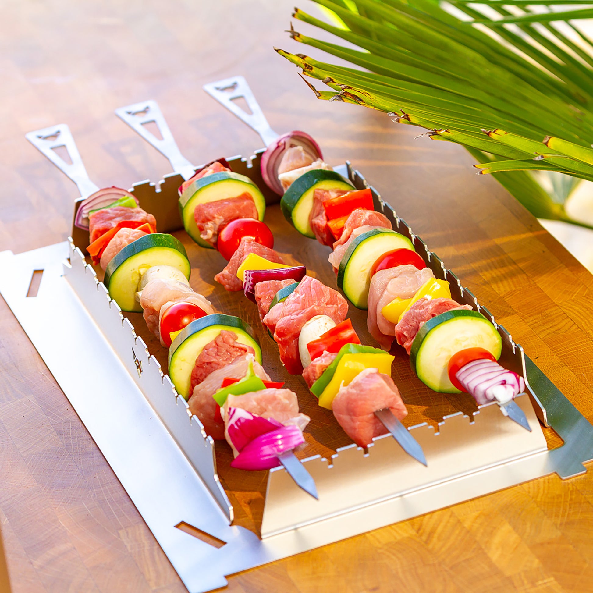 Grillspießhalter mit 3 langen Grillspießen die mit Fleisch und buntem Gemüse zum Grillen vorbereitet sind.