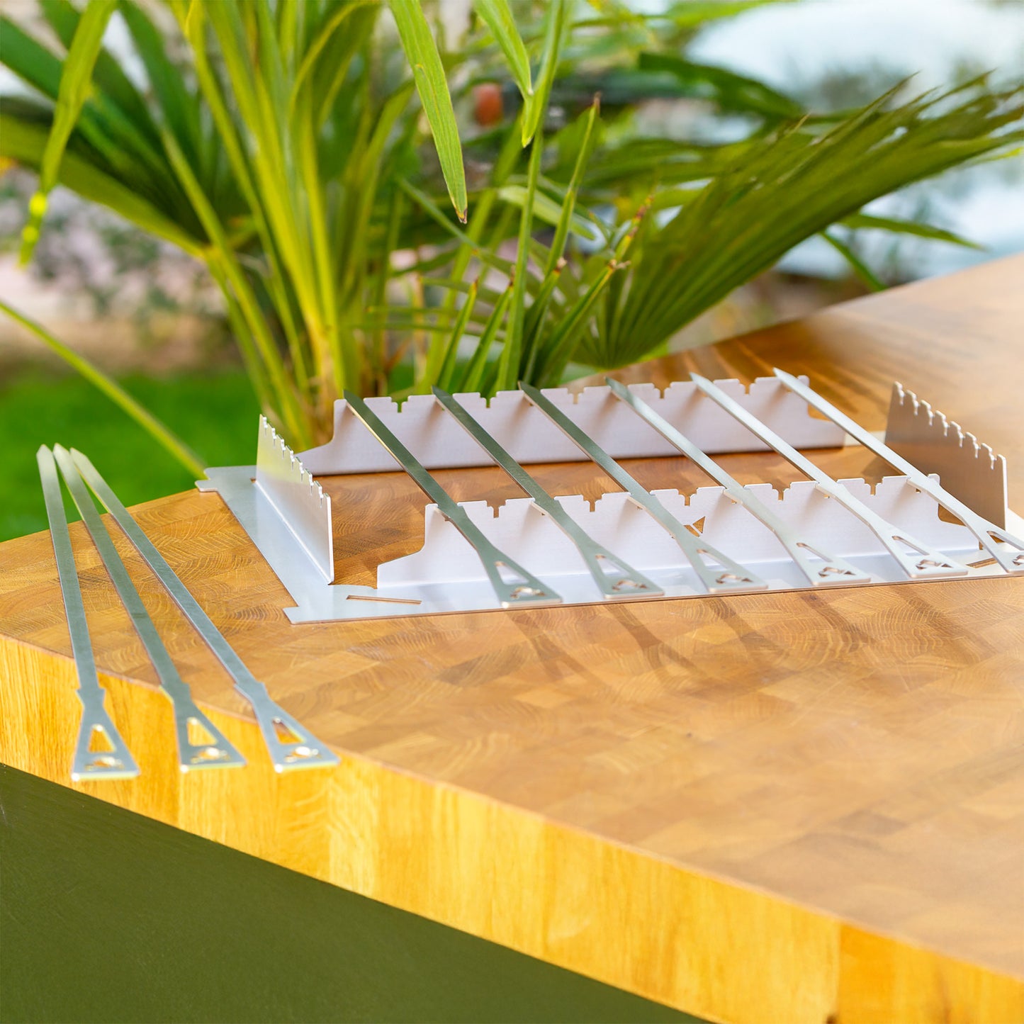 Grillspießhalter mit 6 kurzen und 3 langen Grillspießen liegt auf einem Holztisch.
