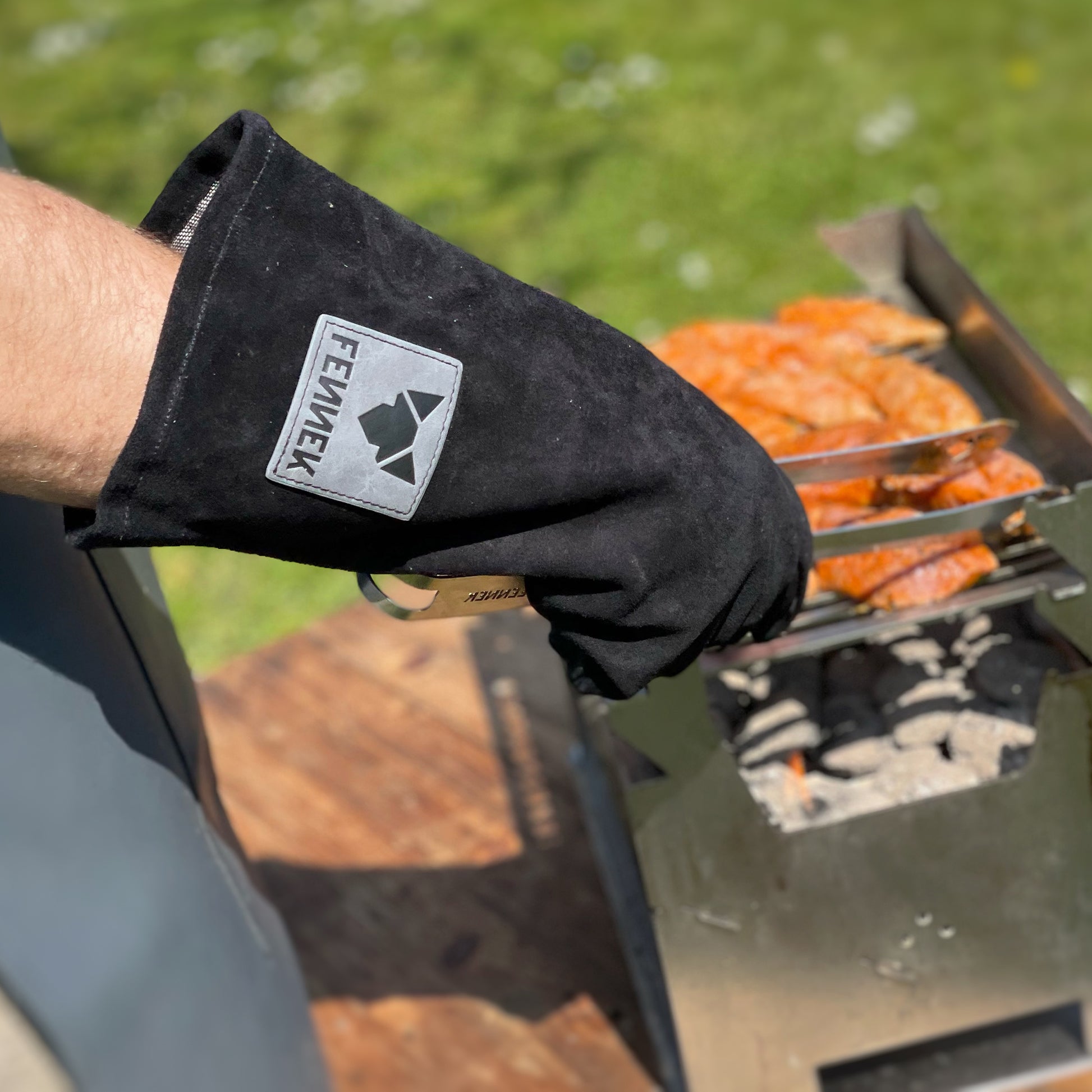 Schwarzer Leder-Grillhandschuh beim Grilleinsatz, wendet mit der Grillzange das Fleisch am Holzkohlegrill