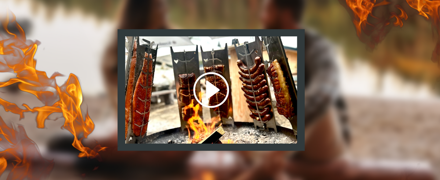 ild zeigt einen kleinen Bildausschnitt auf welchem sechs FENNEK Flammlachshalter zu sehen sind, unter anderem mit Lachs, Würstchen und Rippchen. Links und rechts im Bild sieht man Flammen.