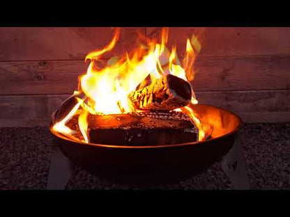 FENNEK Feuerschale Rustic mit loderndem Feuer in Abenddämmerung, steht auf Kiesbett vor einem Holzzaun