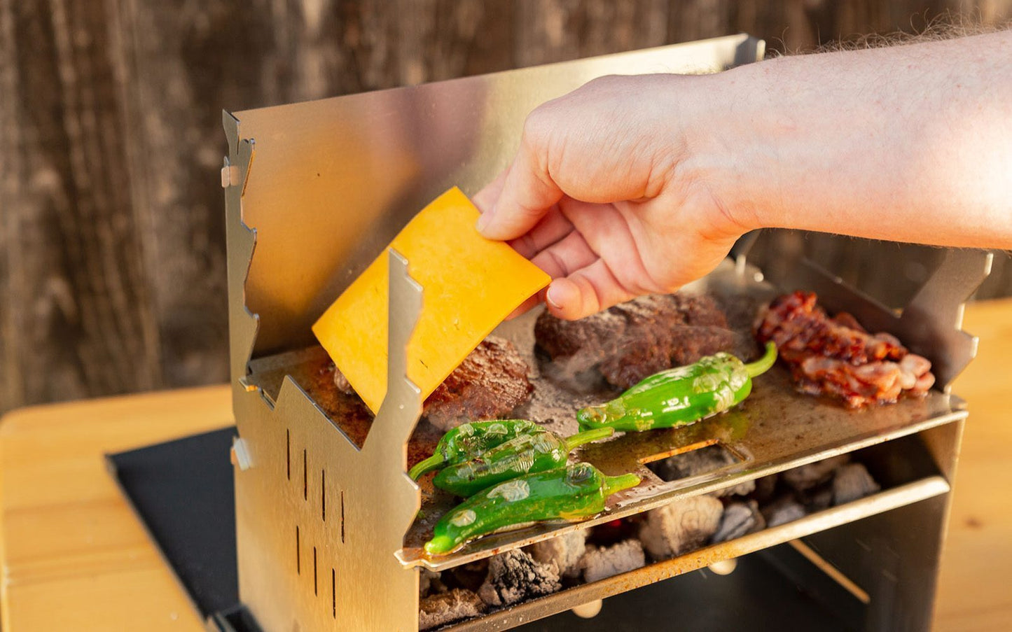 Zubereiten von Burger auf einer Plancha für den FENNEK Grill. Eine Hand legt Käse auf das Patty
