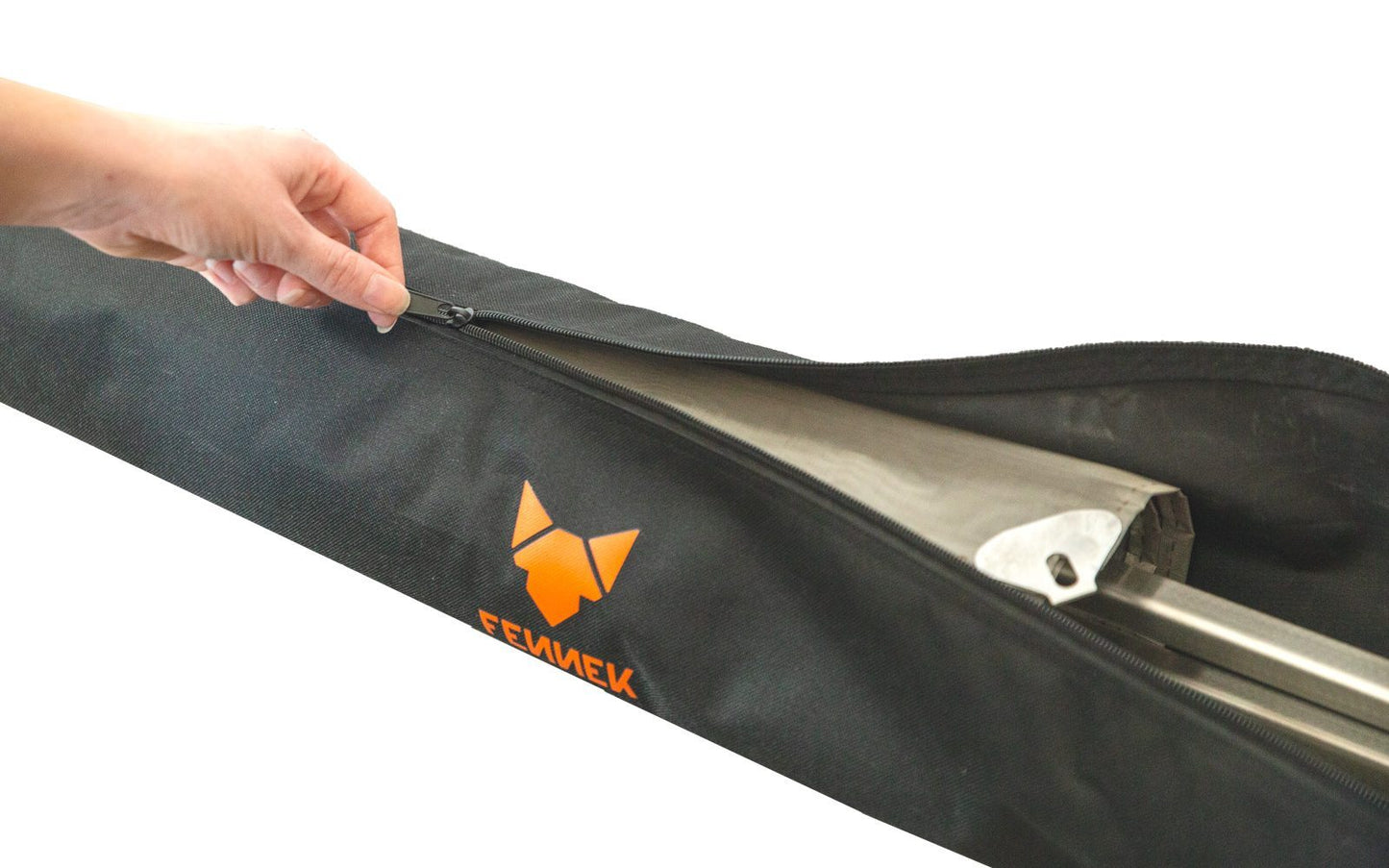 Eine Hand öffnet den Reißverschluss einer schwarzen Nylon-Tasche mit FENNEK Logo-Aufdruck in orange und darin ist das verpackte Feuernetz zu sehen.