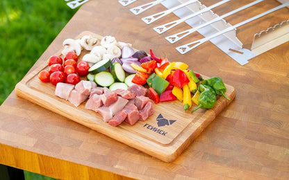 Vorbereitetes, kleingeschnittenes buntes Gemüse und Fleisch auf dem Schneidebrett aus Holz mit FENNEK Logo-Branding rechts unten..