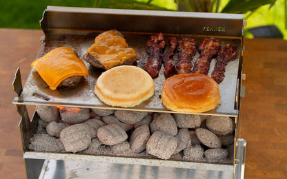 Zubereitung von Cheeseburger und Bacon auf einer Edelstahl Planchaplatte die auf dem Holzkohlegrill aufliegt und mit Holzkohlebriketts betrieben wird.