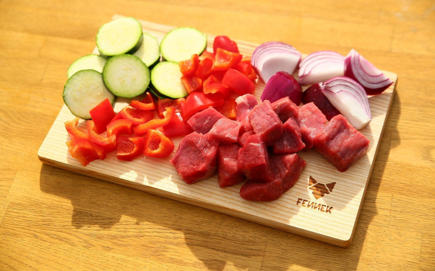 Kleingeschnittenes Rindfleisch und Gemüse auf einem Schneidebrett mit FENNEK Logo-Branding rechts unten
