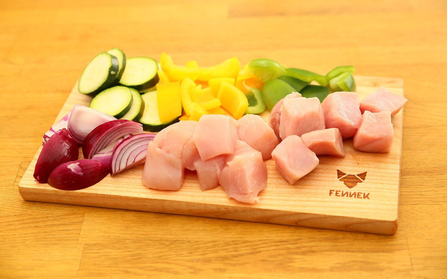 verschiedenes Gemüse und Fleisch, geschnitten auf einem hellen Holzbrett mit FENNEK Logo-Branding rechts unten