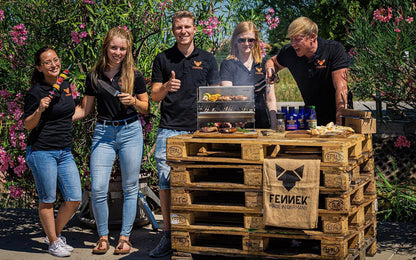 Das Team von FENNEK beim Grillen mit einem Grill auf einem Stapel Holzpaletten