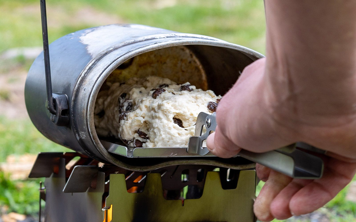 Die Multischale im Einsatz als Backblech, darauf ein Teig mit Rosinen, beim Hineinschieben in ein Kochgeschirr das vom Hobokocher befeuert wird.