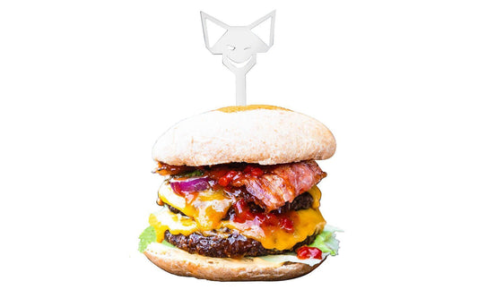 Edelstahl Burgerspieß mit FENNEK-Kopf-Griff steckt im saftigen, Doppel-Cheeseburger mit gebratenem Bacon und Salat, vor weißem Hintergrund