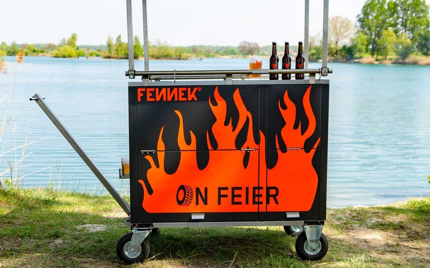 Seitenansicht des FENNEK Bollerwagen mit Deichsel vor einem See bei sonnigem Wetter