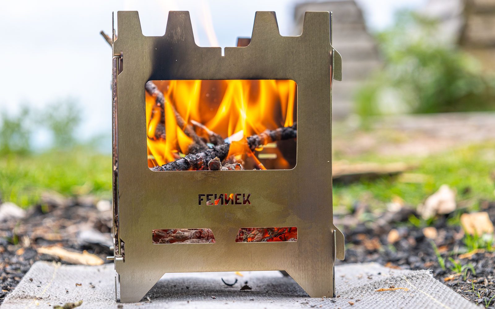 Edelstahl Hobokocher auf einer Hitzschutzmatte in der Natur im Einsatz mit Blick durch die Frontöffnung auf das brennenden Holz
