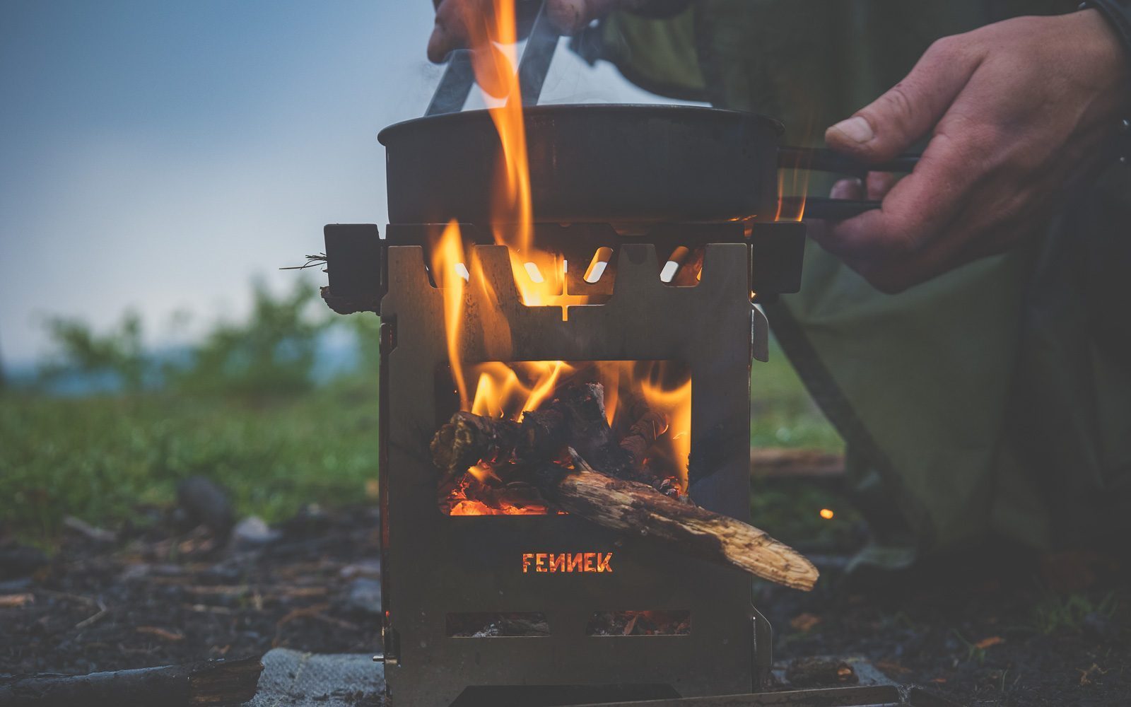 Hobokocher mit brennendem Holz im Einsatz, darauf eine Pfanne in der gerade Essen zubereitet wird in der Natur