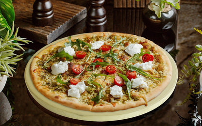 Pizzastein mit einer frisch gebackenen Pizza darauf die mit Käse, Rucolasalat und Tomaten belegt ist.